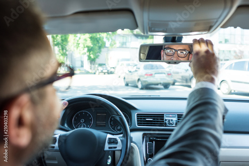 partial view of businessman in eyeglasses looking at rear view mirror in car photo