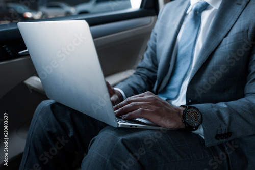 cropped shot of businessman in using laptop on backseat in car