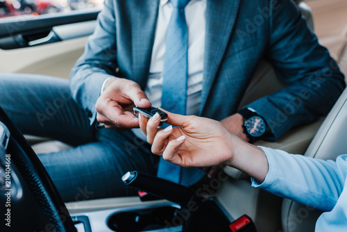 cropped shot of businessman giving car keys to colleague at driver seat in car