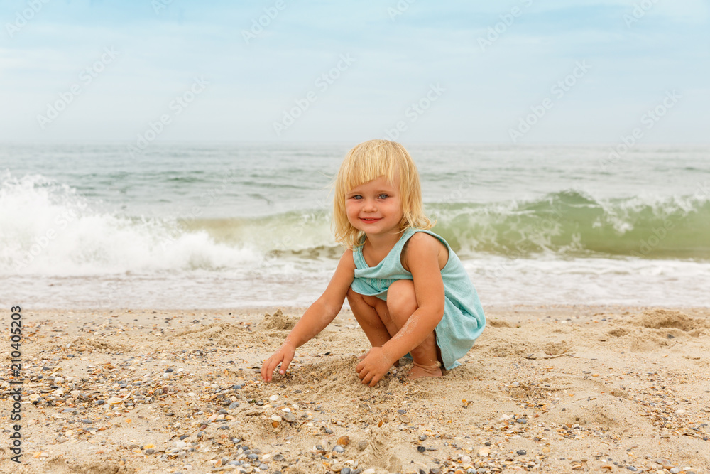 A little girl with bright hair plays with the sand on the sea beach. A little girl with bright hair plays with the sand on the sea beach.