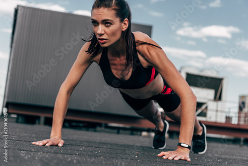 concentrated sportswoman doing push up on asphalt in city