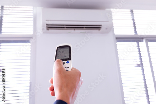 Air conditioner with remote controller,inside the room with man operating remote controller.