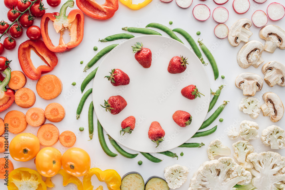 fresh ripe strawberries on round white plate and organic vegetables isolated on white