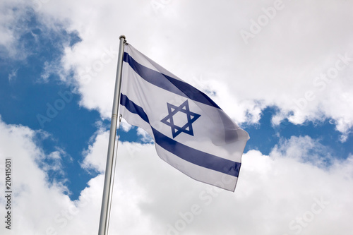 Flag of Israel waving in the wind on flagpole against the sky with clouds on sunny day, close-up