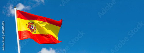 Flag of Spain waving in the wind on flagpole against the sky with clouds on sunny day, banner, close-up photo