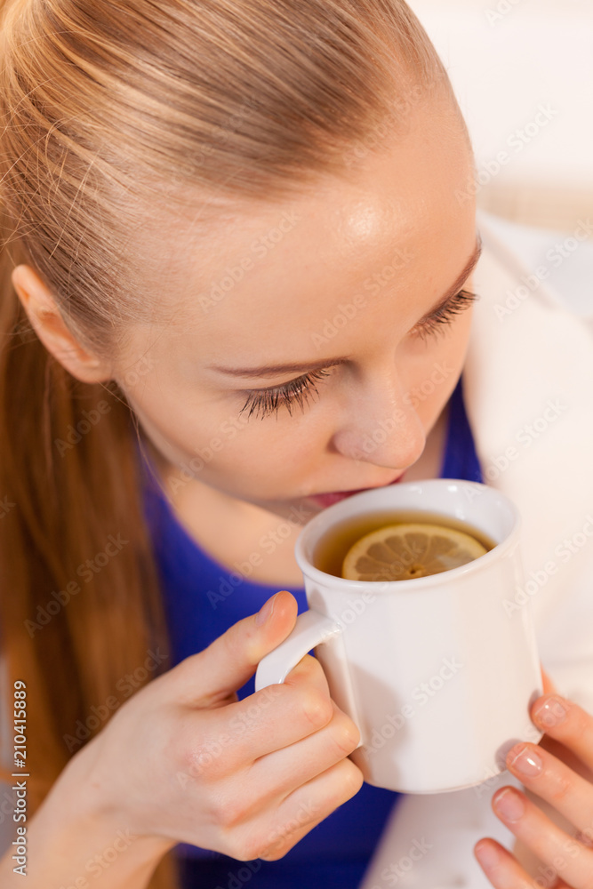 Woman lying on sofa under blanket drinking tea Woman lying on sofa under blanket drinking tea