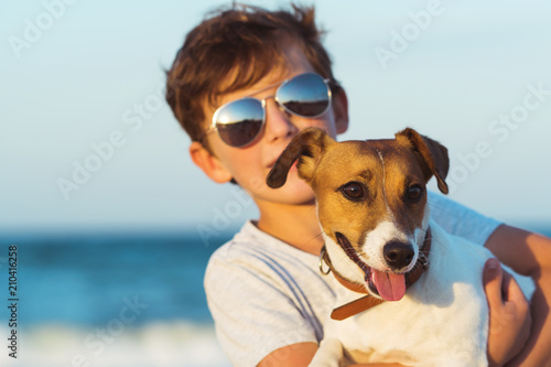 Happy boy hugging his dog breed Jack russell at the seashore against a blue sky close up at sunset. Best friends rest and have fun on vacation, play in the sand against the sea