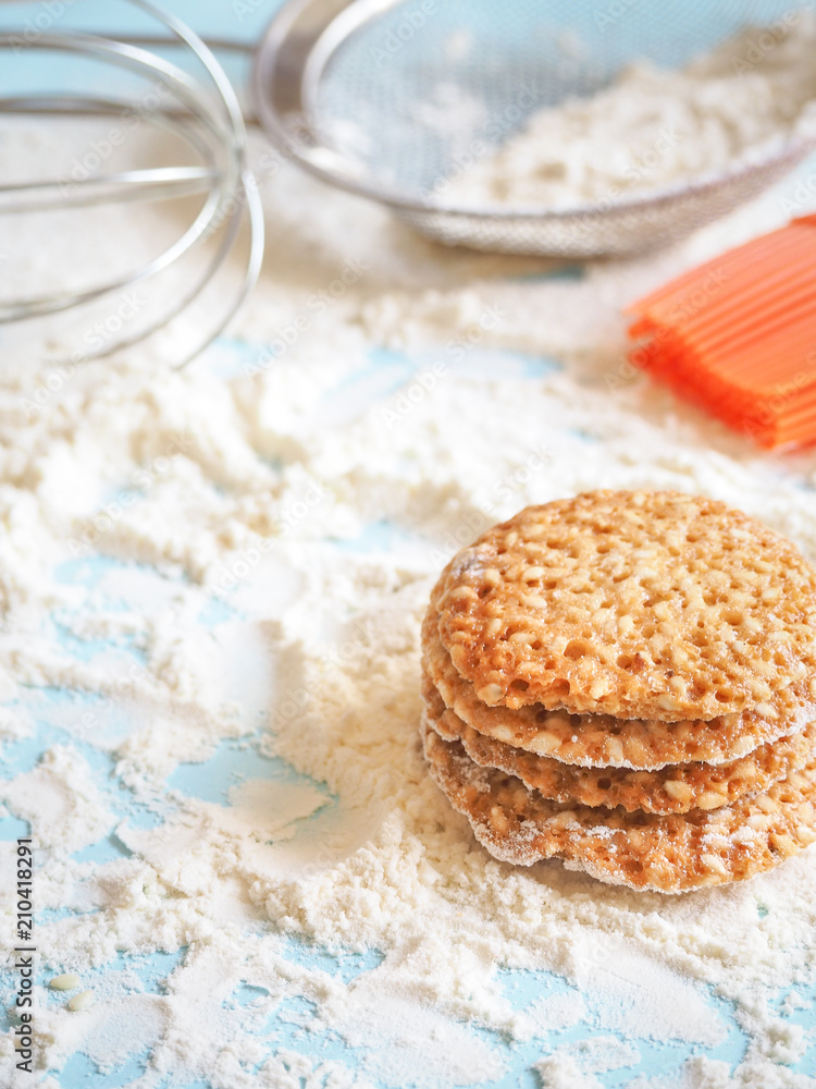 top view of product set for cooking cookies, kitchenware and several round cookies with sesame on a blue wooden table top view of product set for cooking cookies, kitchenware and several round cookies with sesame on a blue wooden table