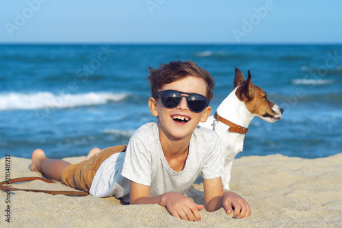 Happy boy hugging his dog breed Jack russell at the seashore against a blue sky close up at sunset. Best friends rest and have fun on vacation, play in the sand against the sea © marina_larina