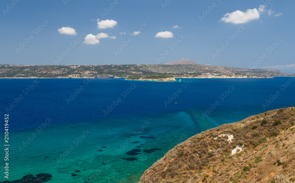 Obraz premium the rocky shore of the sea. the turquoise sea and mountains on blue sky background with clouds. Elafonisi, Crete, Greece
