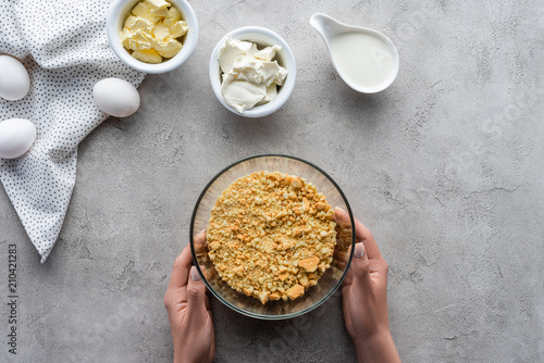 Photos cropped shot of woman holding bowl with crushed cookies for pie on grey tabletop