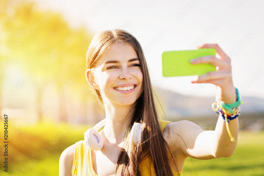 Cute cheerful teenage girl vlogging outdoors on sunny summer day. Young woman taking a selfie in park in spring Cute cheerful teenage girl vlogging outdoors on sunny summer day. Young woman taking a selfie in park in spring