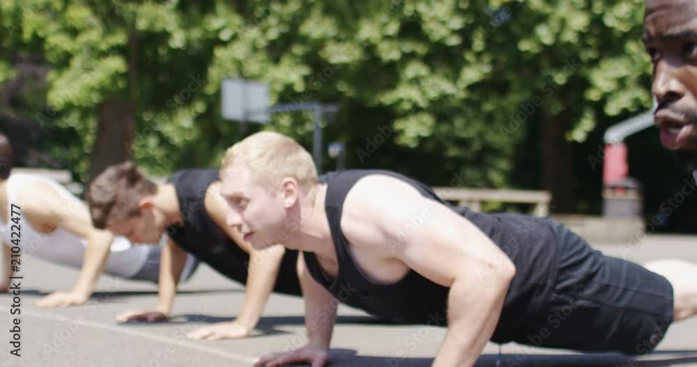 Four healthy young men doing push ups in a park, in slow motion Four healthy young men doing push ups in a park, in slow motion