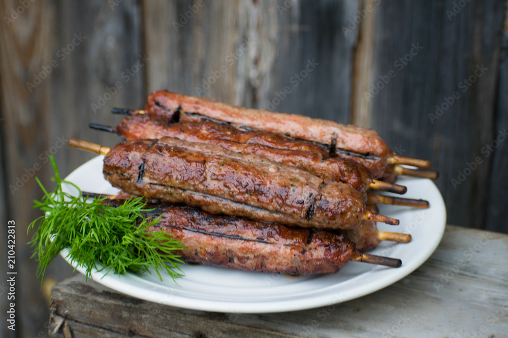 Lulya kebab from meat on a white plate and wooden board with dill.
