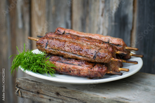 Lulya kebab from meat on a white plate and wooden board with dill.