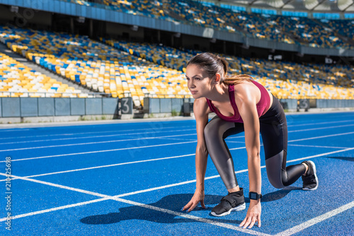 fit female runner in start position on running track at sports stadium