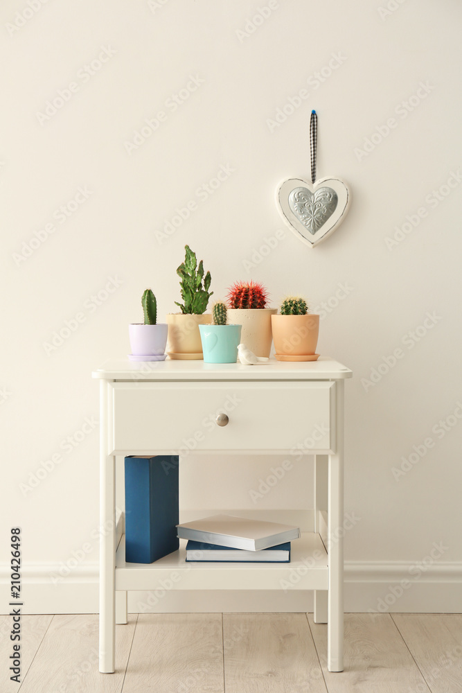 Fototapeta premium Beautiful cacti on table near light wall