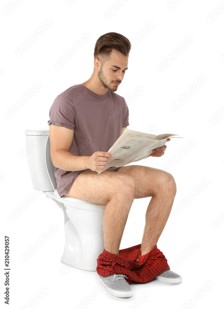 Young man reading newspaper while sitting on toilet bowl. Isolated on
