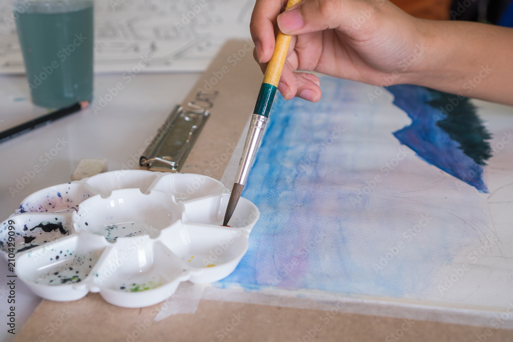 Fototapeta premium Student's hand with brush drawing on paper for creation picture abstract of watercolor painting with bamboo brush in Art subject classroom secondary education in Thailand
