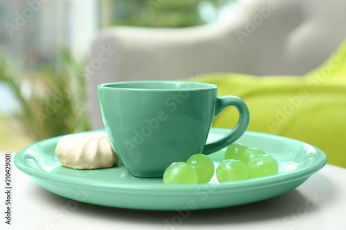 Green cup and plate with mint candies on table against blurred background