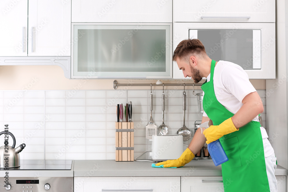 Young man in uniform cleaning kitchen counter Young man in uniform cleaning kitchen counter