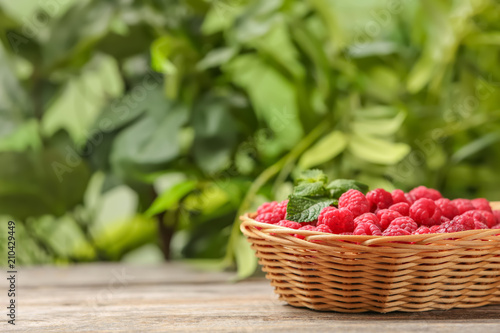 Wicker basket with ripe aromatic raspberries on table against blurred background