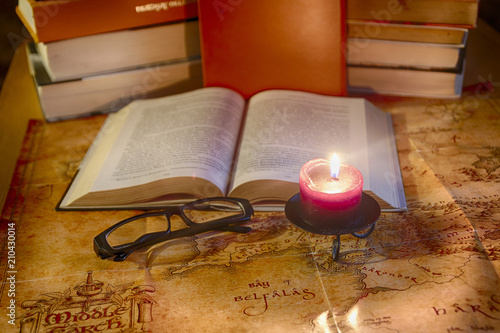 Vintage still life: a book, glasses and a burning candle against the background of stacks of books and an ancient world map