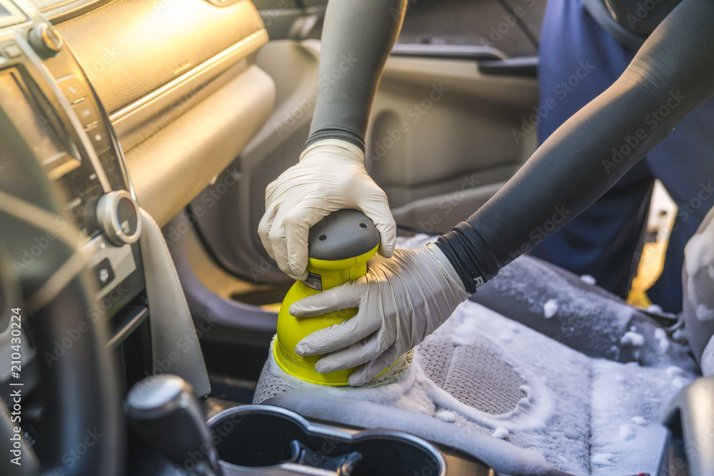 a man cleaning car interior by use foam chemical and scrubbing machine.  Stock Photo | Adobe Stock