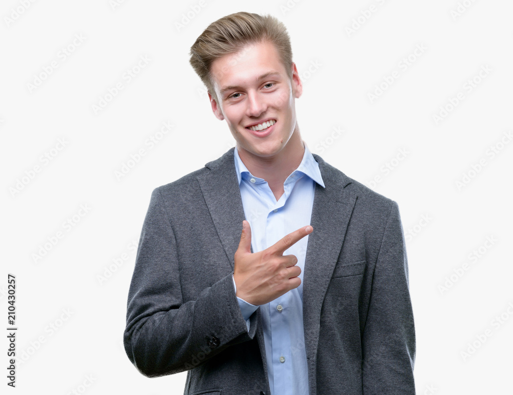 Young handsome blond business man cheerful with a smile of face pointing with hand and finger up to the side with happy and natural expression on face looking at the camera. Young handsome blond business man cheerful with a smile of face pointing with hand and finger up to the side with happy and natural expression on face looking at the camera.