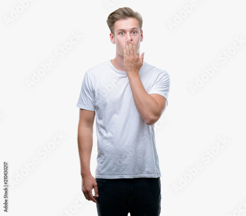 Young handsome blond man cover mouth with hand shocked with shame for mistake, expression of fear, scared in silence, secret concept