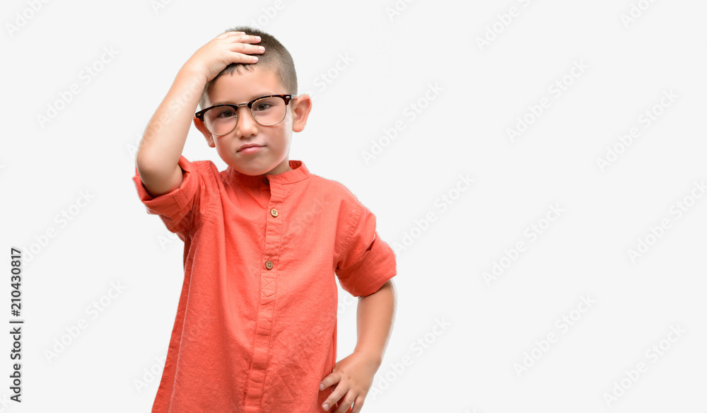 Dark haired little child wearing glasses stressed with hand on head, shocked with shame and surprise face, angry and frustrated. Fear and upset for mistake. Dark haired little child wearing glasses stressed with hand on head, shocked with shame and surprise face, angry and frustrated. Fear and upset for mistake.