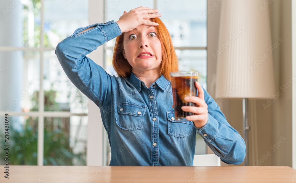 Φωτογραφία Redhead woman holding soda refreshment stressed with hand on head, shocked with shame and surprise face, angry and frustrated