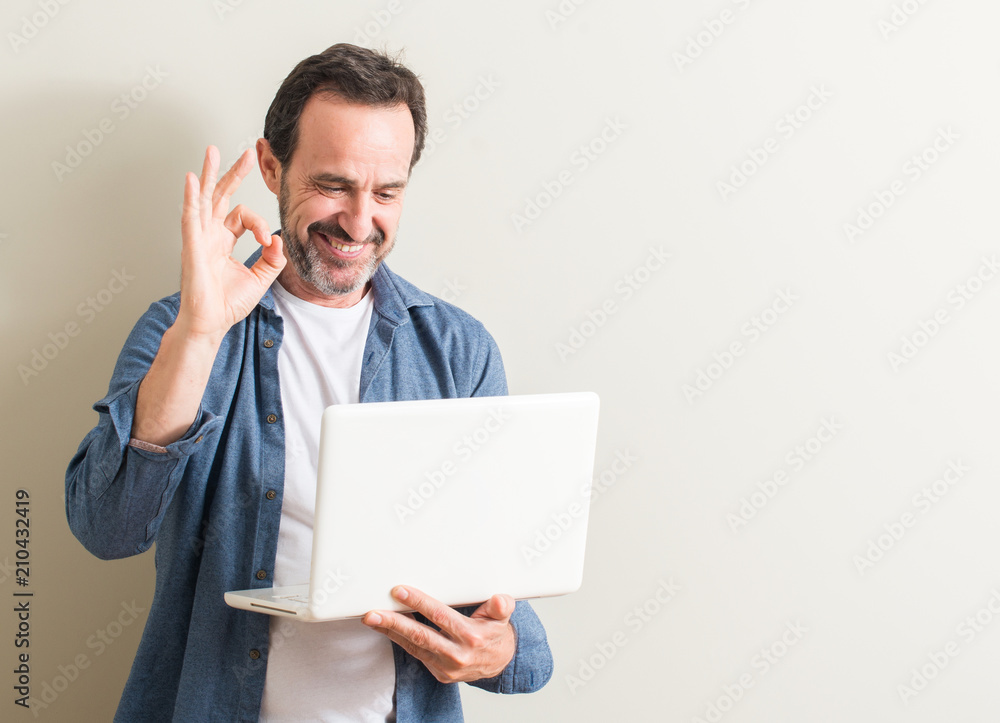 Senior man using laptop computer doing ok sign with fingers, excellent symbol Senior man using laptop computer doing ok sign with fingers, excellent symbol
