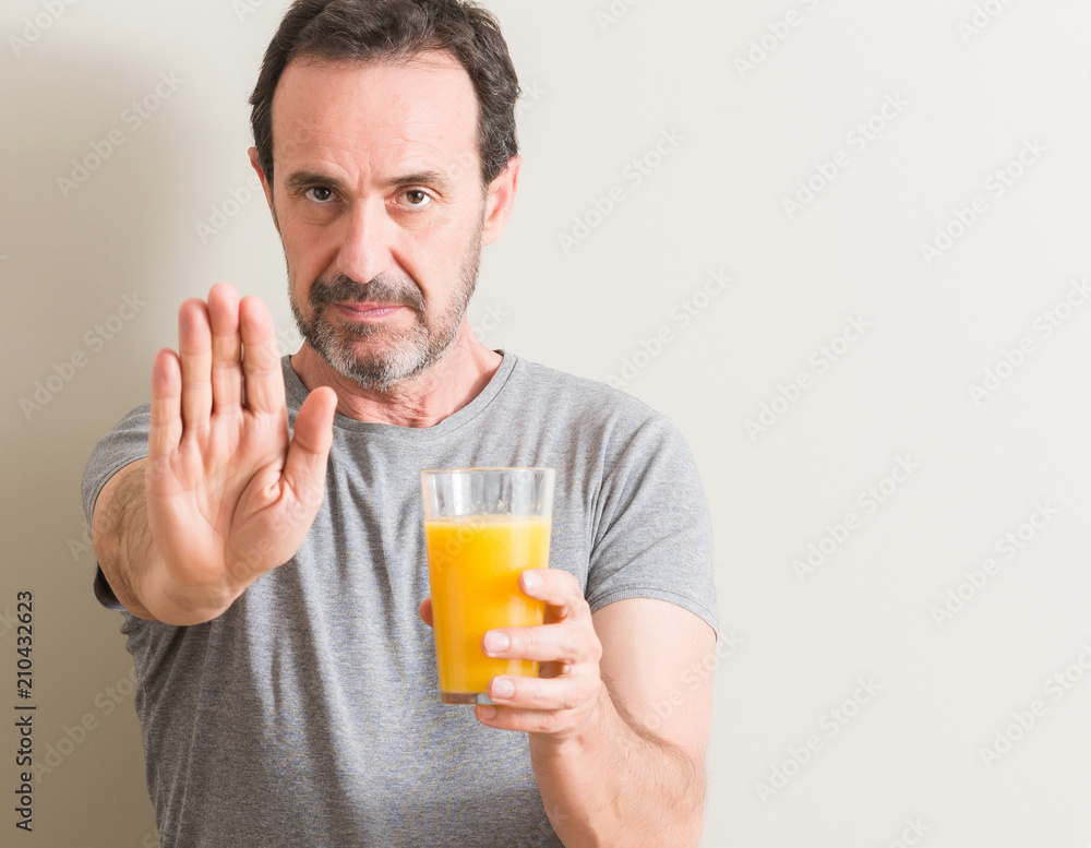 Senior man drinking orange juice in a glass with open hand doing stop sign with serious and confident expression, defense gesture Senior man drinking orange juice in a glass with open hand doing stop sign with serious and confident expression, defense gesture