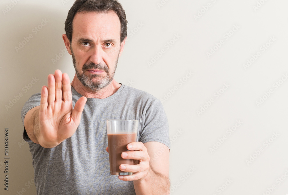 Senior man drinking chocolate milk shake with open hand doing stop sign with serious and confident expression, defense gesture Senior man drinking chocolate milk shake with open hand doing stop sign with serious and confident expression, defense gesture