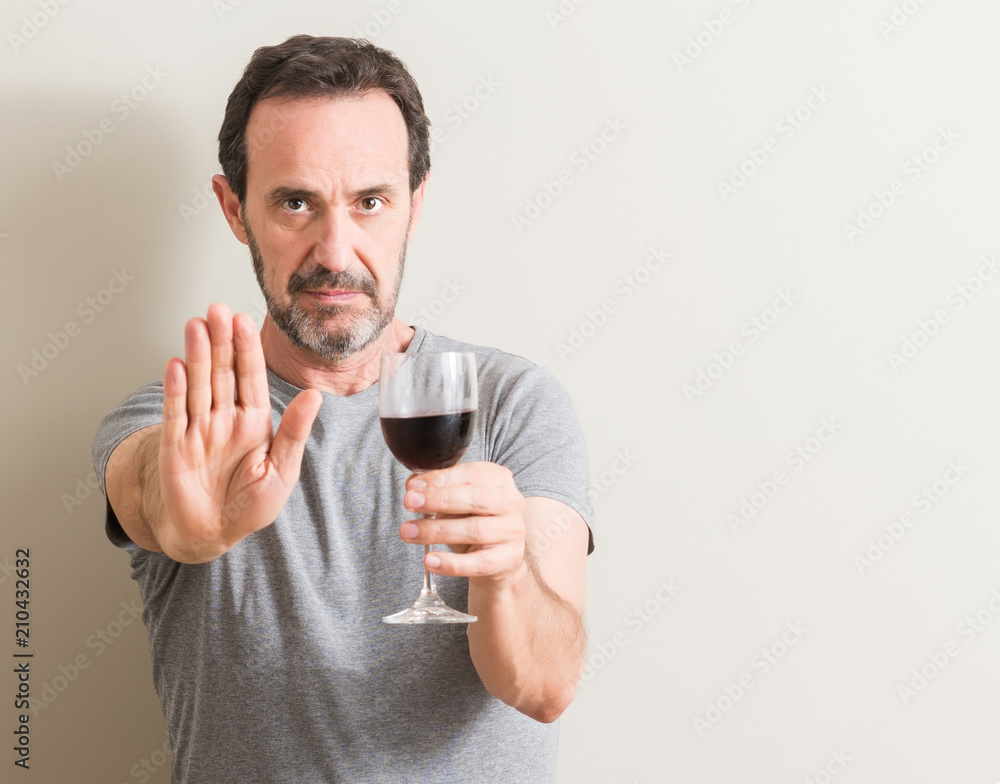 Senior man drinking red wine in a glass with open hand doing stop sign with serious and confident expression, defense gesture Senior man drinking red wine in a glass with open hand doing stop sign with serious and confident expression, defense gesture