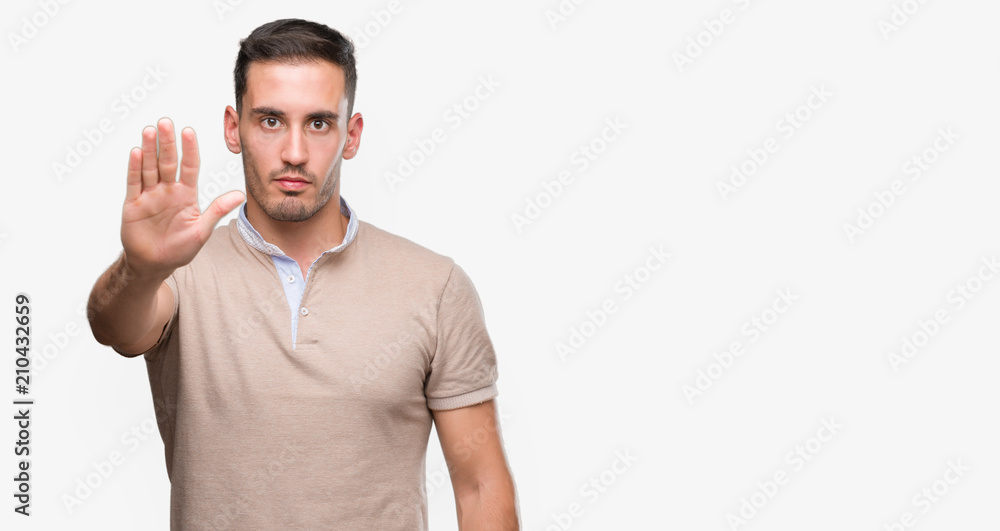 Handsome young man with open hand doing stop sign with serious and confident expression, defense gesture Handsome young man with open hand doing stop sign with serious and confident expression, defense gesture