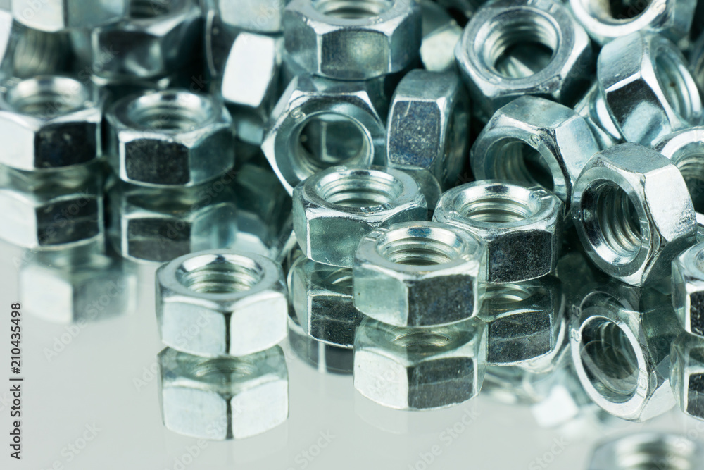Stack of shiny nuts on a mirror background. Pile of fastener with a threaded hole that forms a connection with a screw, bolt or stud Stack of shiny nuts on a mirror background. Pile of fastener with a threaded hole that forms a connection with a screw, bolt or stud