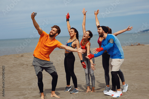Group of young sports people doing seflie on the beach by the sea
