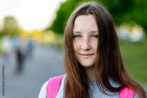 A beautiful child, teenage girl. Summer in nature. Close-up portrait. Blue eyes freckles on face. Smiles happily. Free space for text. Concept of rest. Emotion of pleasure.