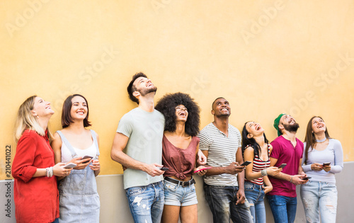 Multiracial friends having fun using smartphone at wall on university college break - Young people addicted by mobile smart phones - Technology concept with always connected millennials - Filter image photo