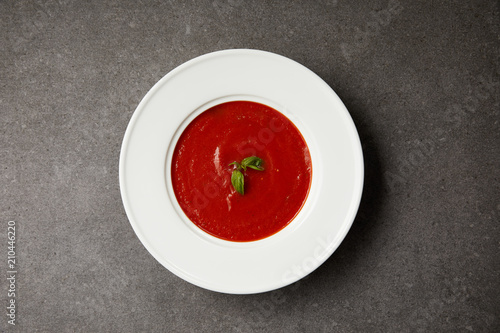 Obraz na plátně top view of red tomato soup with basil in white plate on grey table