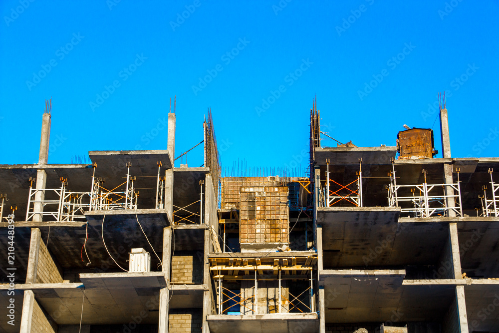 Fototapeta premium The frame of a highrise building under construction without walls against a blue clear sky. Abandoned building.