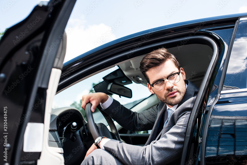 pensive businessman in eyeglasses looking away while sitting in car