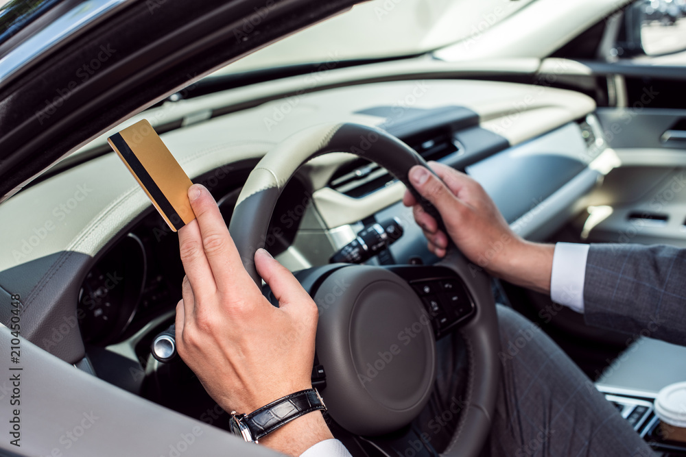 partial view of businessman with credit card in hand sitting at steering wheel in car