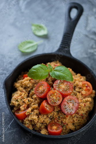 Cuscus with cherry tomatoes and spices in a cast-iron pan, selective focus