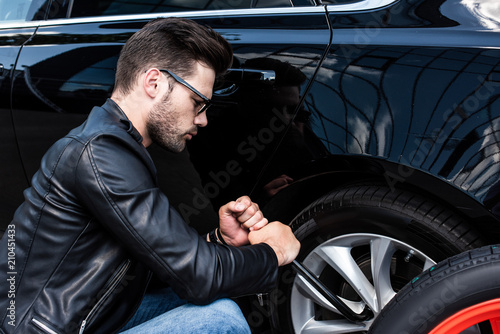 focused young man in sunglasses using wheel spanner for wheel replacement at street © LIGHTFIELD STUDIOS