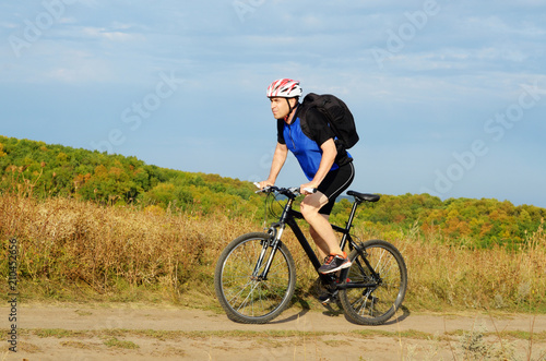 Male cyclist with backpack driving by rural dirt road outdoors