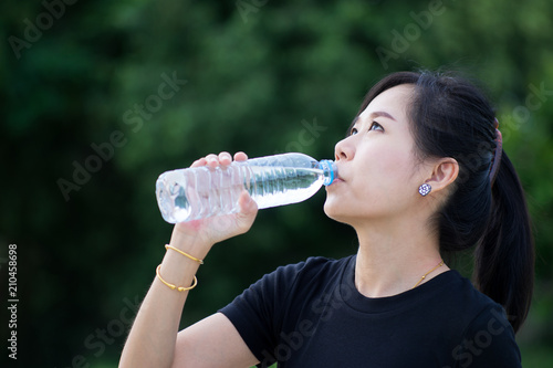 Asian woman drinking water with green nature background.