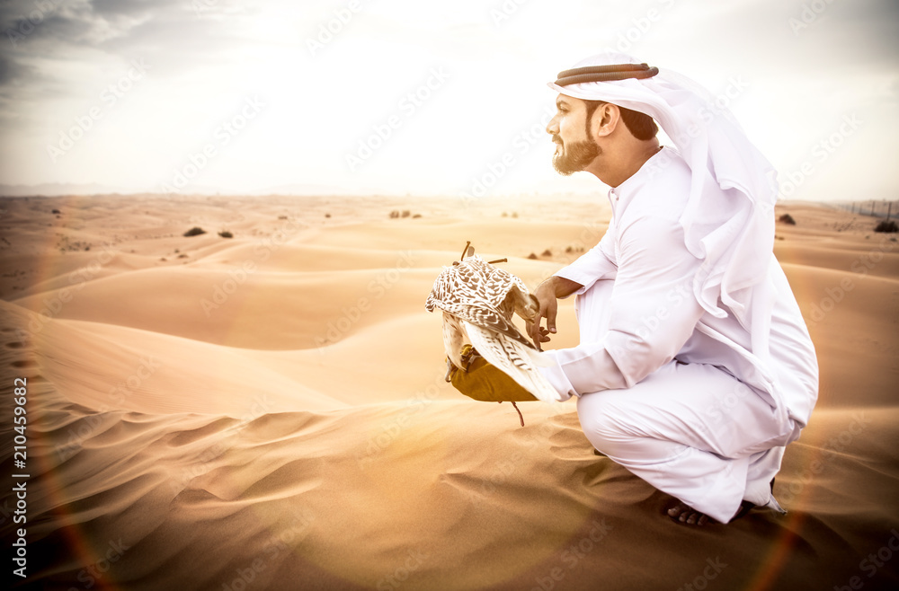 Obraz premium Arabski mężczyzna w tradycyjnych emirackich strojach spacerujący po pustyni ze swoim sokołem